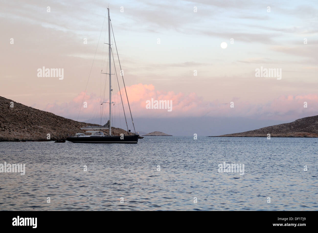 Un voilier amarré dans le port de Port Halki Chalki Emporio au coucher du soleil avec la Lune se levant sur la Mer Égée Grèce Dodecanses Banque D'Images