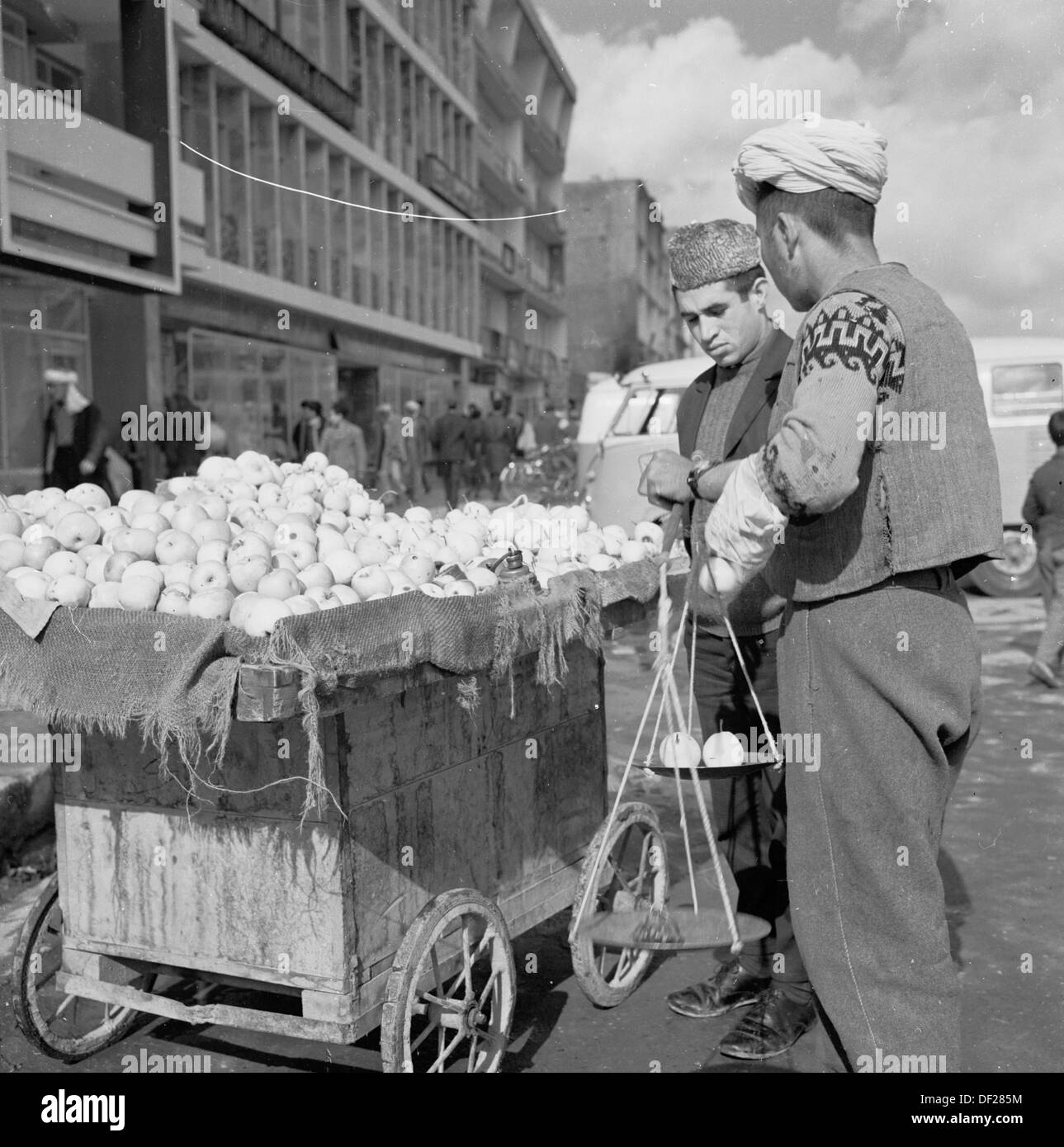 Photo historique, années 1950 par J Allan Cash, montrant un vendeur de rue afghan par sa petite charrette en bois à Kaboul, en Afghanistan, pesant des fruits pour un client. Un temps relativement pacifique pour le pays, cette époque a vu de nouveaux bâtiments construits, quelques pas faits vers la modernisation et faire du pays une société plus ouverte et prospère. Cela s'est terminé dans les années 1970 par une succession d'invasions, d'coups d'Etat et de guerres civiles. Banque D'Images