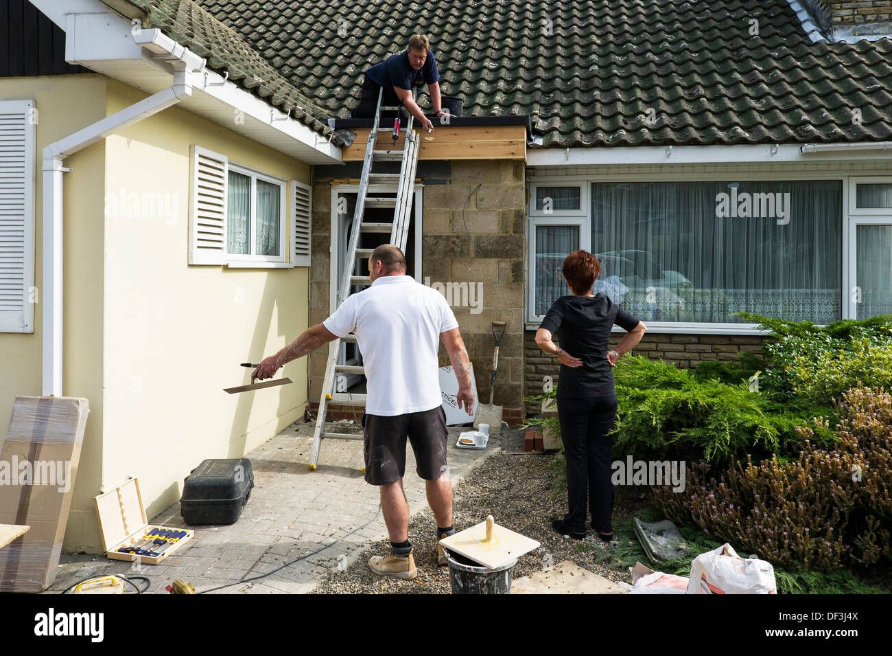 Deux constructeurs travaillant dans une maison d'avoir une discussion avec le maître de maison. Banque D'Images