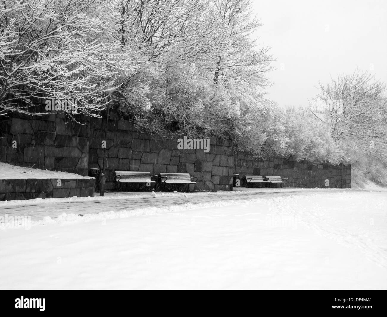 Des bancs le long du mur en pierre dans le parc enneigé Banque D'Images