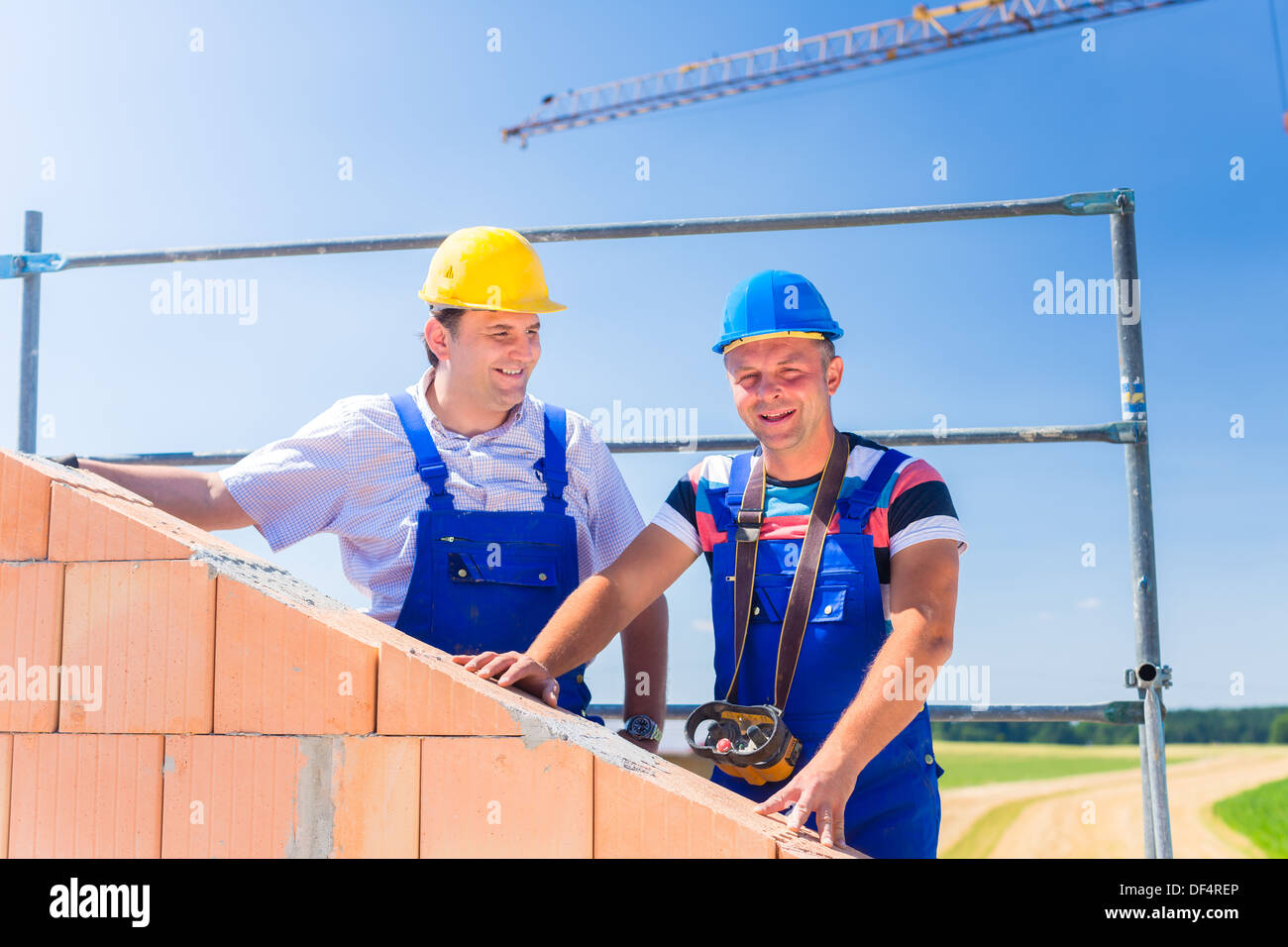 Deux fiers travailleurs du chantier ou maçons debout sur le projet de la maison à l'aide d'une télécommande de grue Banque D'Images