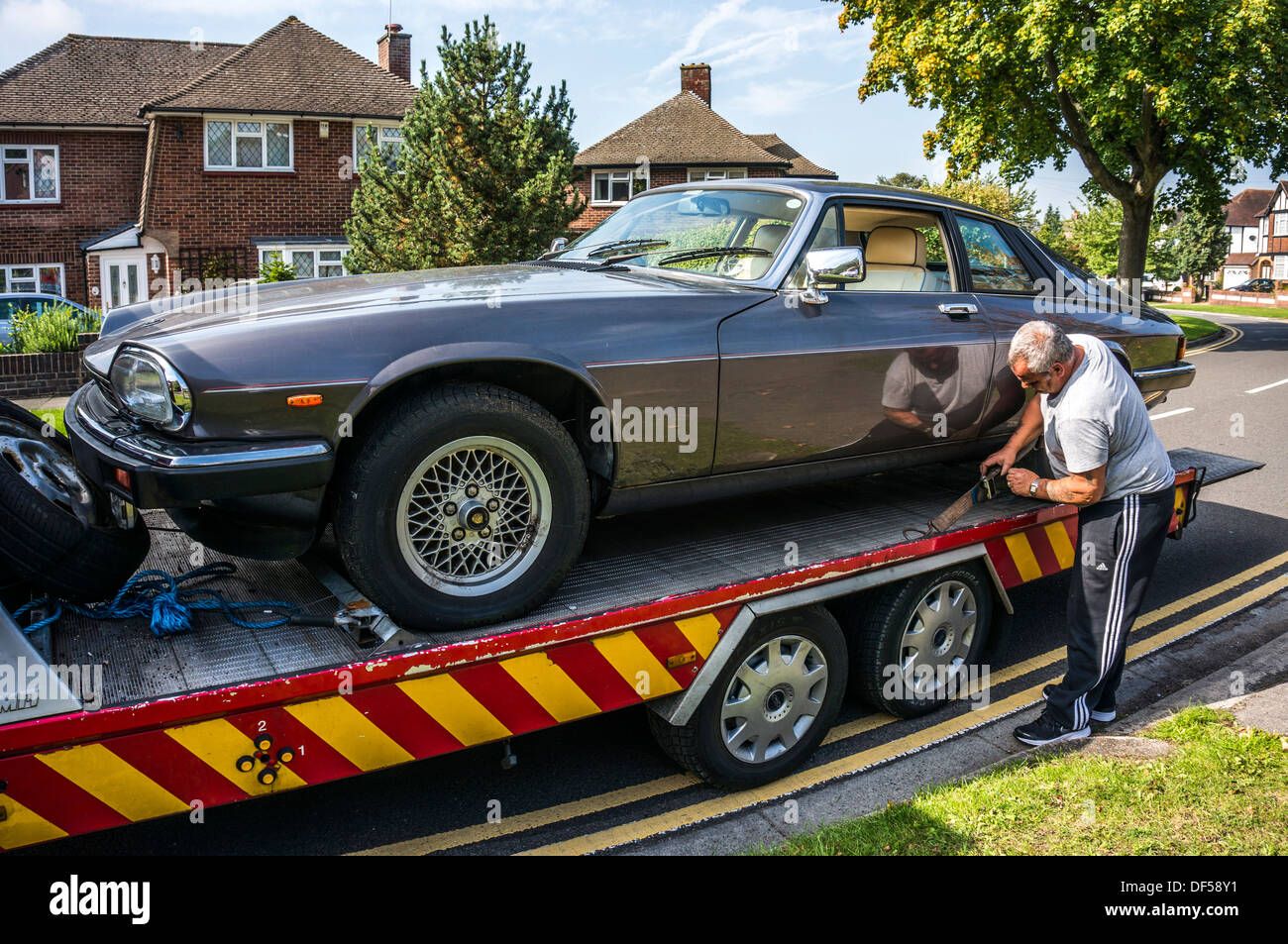 Homme sangles de serrage pour fixer une Jaguar XJS sur son véhicule de récupération, dans and Banstead, Surrey, Angleterre. Banque D'Images