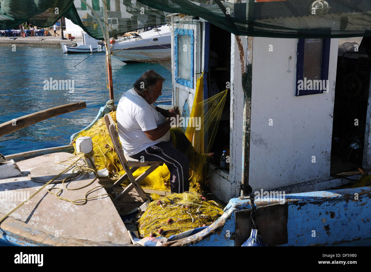 Assis dans son bateau pêcheur réparant les filets de pêche Port Port Halki Chalki Grèce Banque D'Images