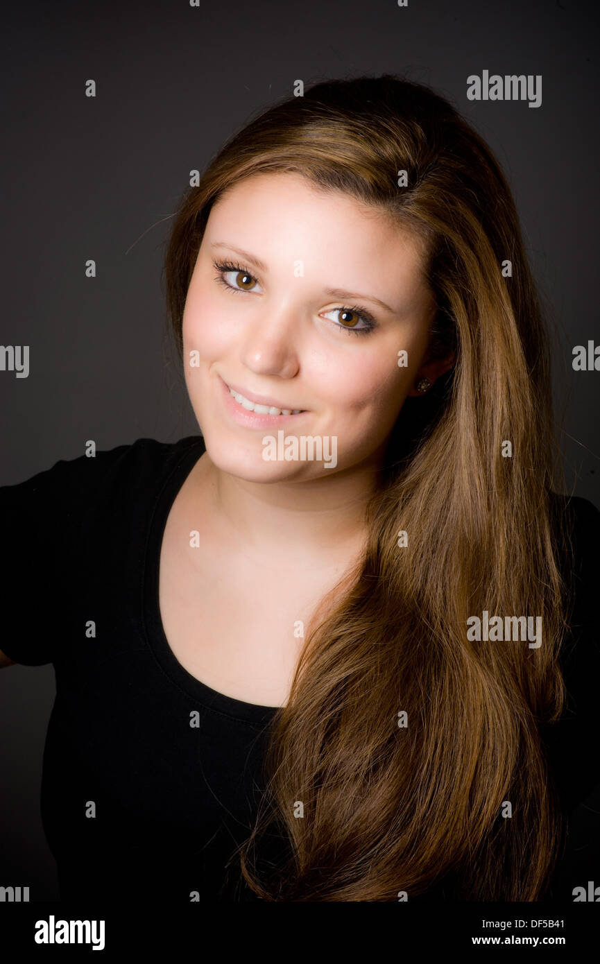 Une jeune femme de race blanche, aux cheveux longs et bruns clair, a balayé son épaule en regardant la caméra sourire. Banque D'Images