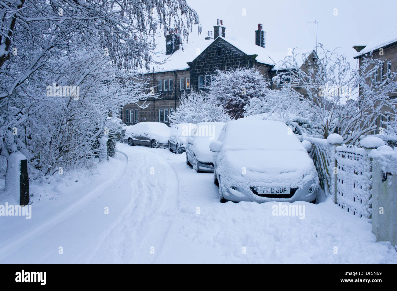 Scène d'hiver avec des voitures garées à l'extérieur de maisons jumelées sur rue résidentielle calme, tous couverts en couverture de neige fraîche - Guiseley, England, UK. Banque D'Images