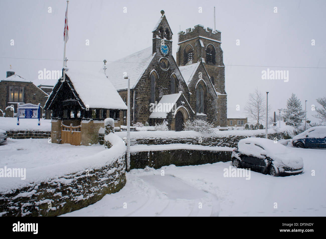 Scène d'hiver froid et gris avec la neige qui tombe sur l'église Saint-Jean (bâtiments et voitures couvert de couche blanche) - Baildon, West Yorkshire, Angleterre, Royaume-Uni. Banque D'Images