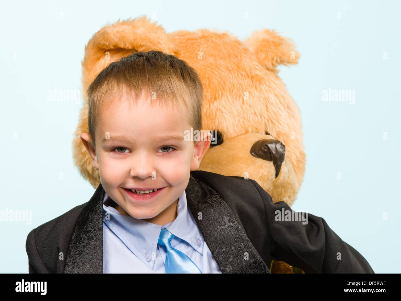 Petit garçon qui pose et jouant avec un ours sur le studio, fond bleu clair Banque D'Images