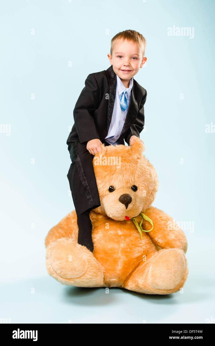 Petit garçon qui pose et jouant avec un ours sur le studio, fond bleu clair Banque D'Images