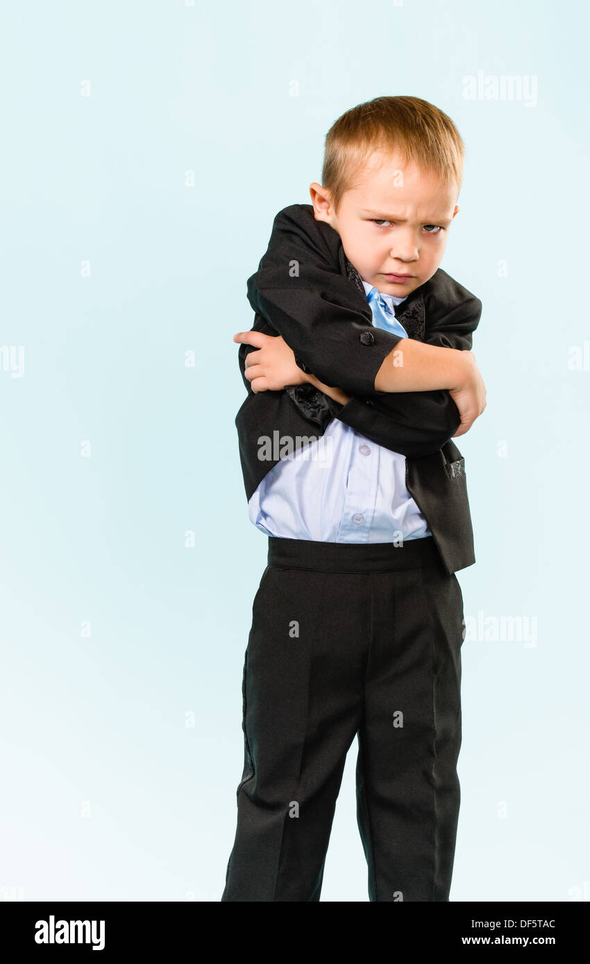 Malheureux petit garçon portant costume, studio shot et fond bleu clair Banque D'Images