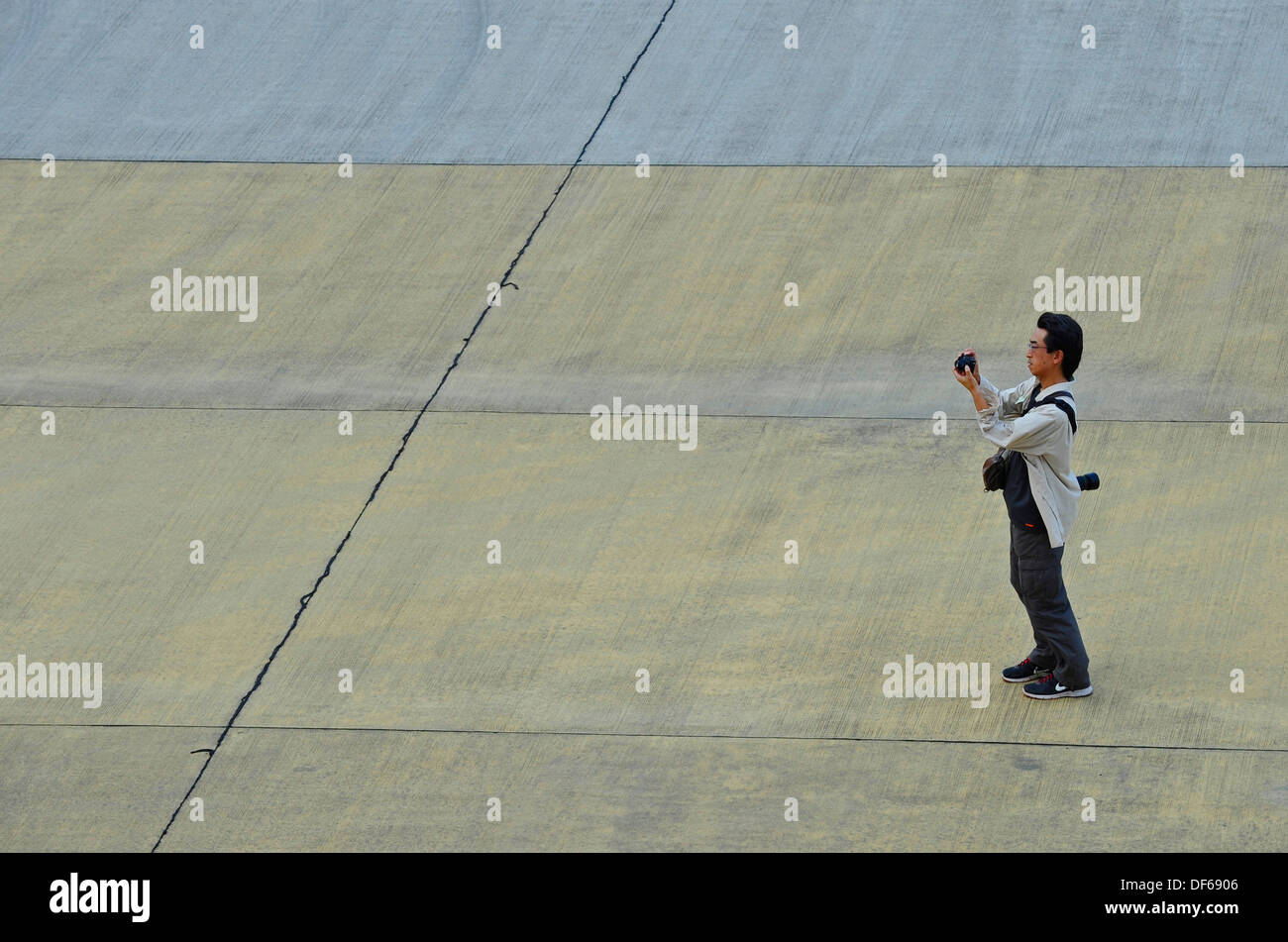 L'homme japonais de prendre des photos tout en se tenant sur un côté quai en béton. Banque D'Images