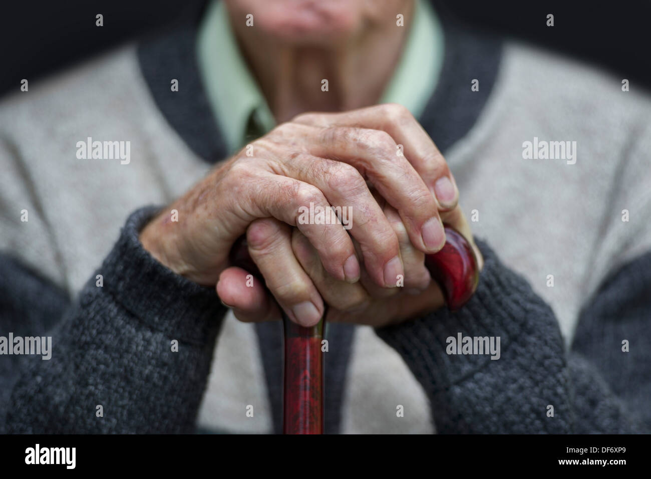 Un vieux retraité siège avec ses mains sur un bâton de marche dans une maison de soins. Banque D'Images