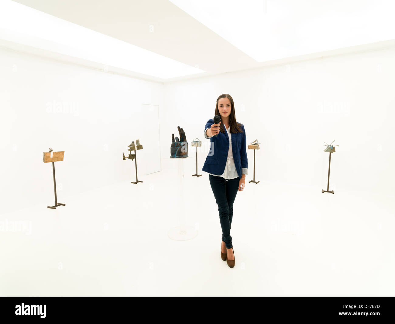 Portrait femme journaliste debout dans une galerie d'art, tenant un micro dans sa main, pour demander une entrevue Banque D'Images