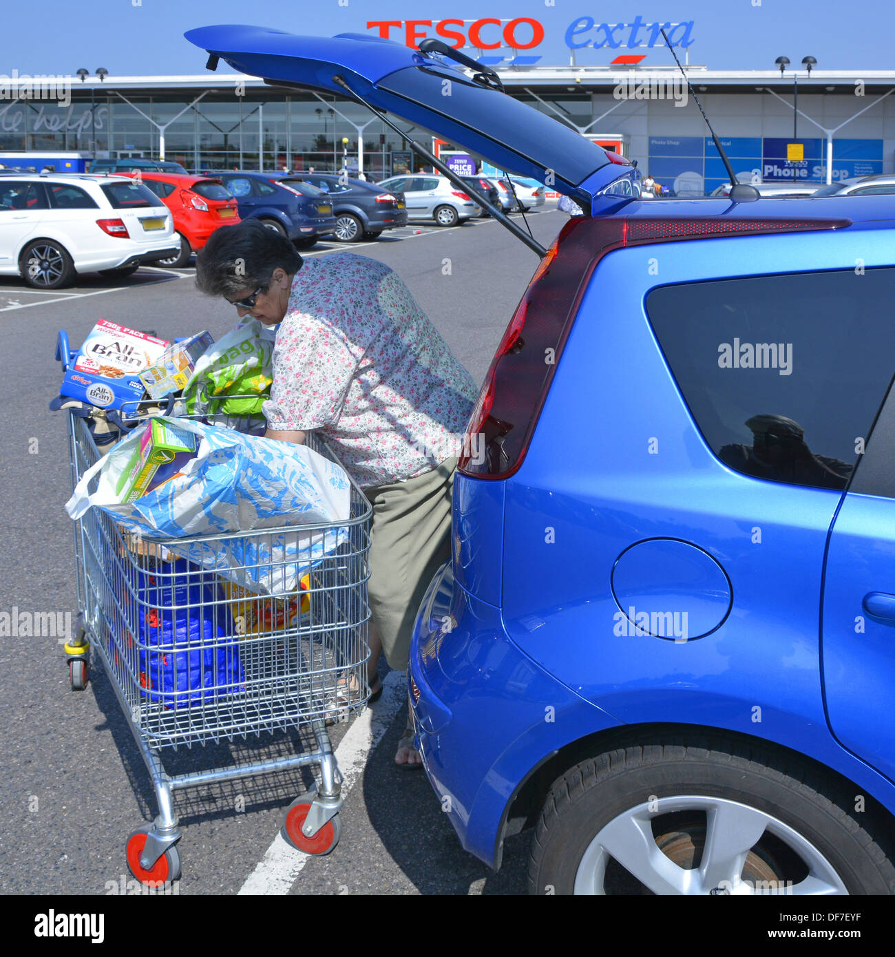Femme Shopper déchargement de nourriture épicerie de Tesco Extra chariot de supermarché et de transfert dans voiture à hayon grande ville de Londres Angleterre Royaume-Uni Banque D'Images