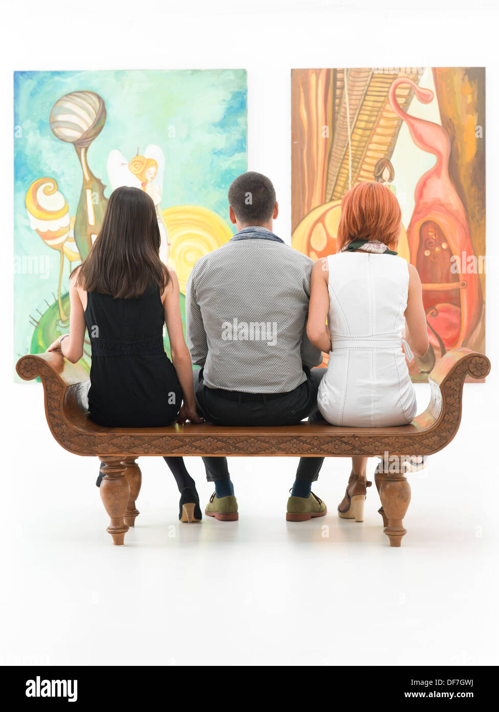 Vue arrière de trois jeunes gens assis sur un banc en bois dans un musée à admirer de grandes peintures Banque D'Images