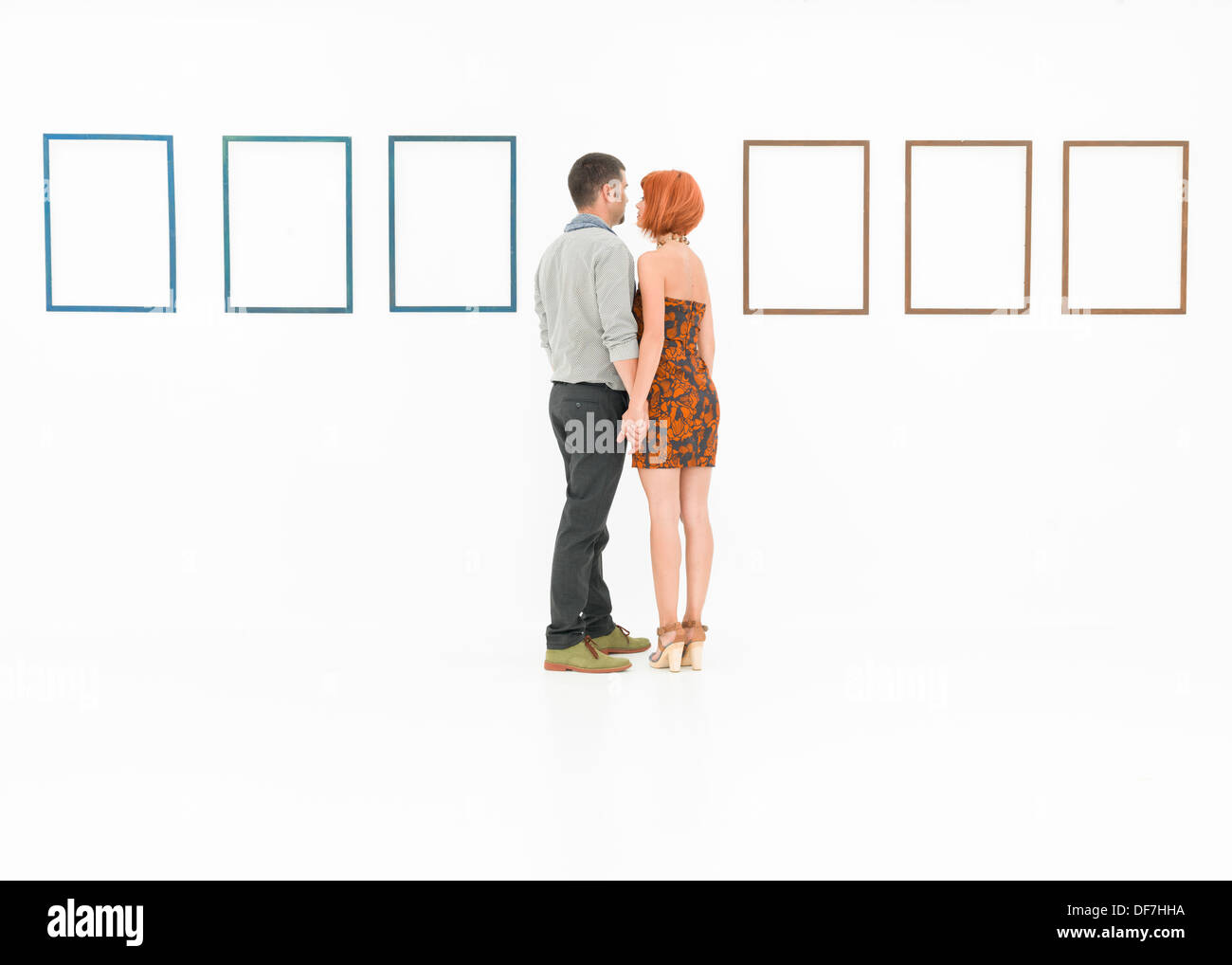 L'homme et la femme se tenant la main en face de cadres vides affichées sur des murs blancs Banque D'Images