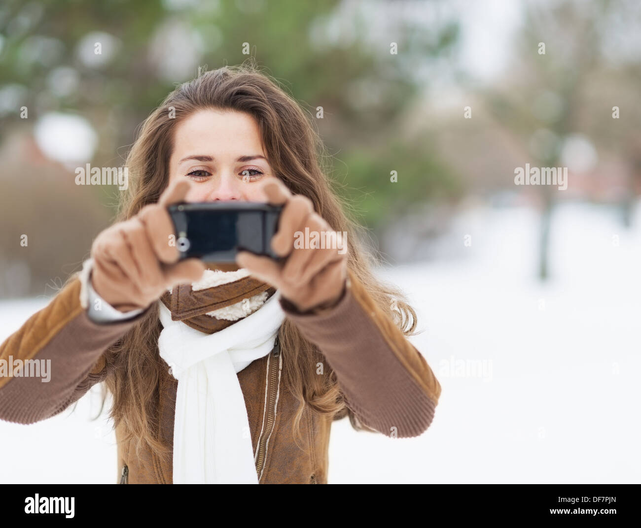 Young woman taking photo using cell phone in winter park Banque D'Images