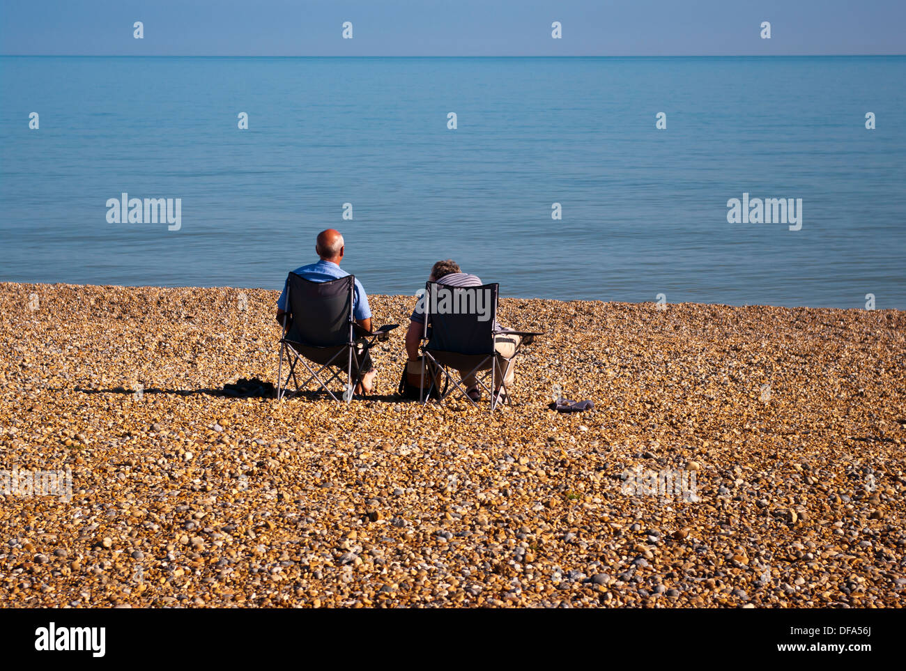 Vue arrière d'un couple de personnes âgées assis sur des chaises de plage face à la mer Banque D'Images