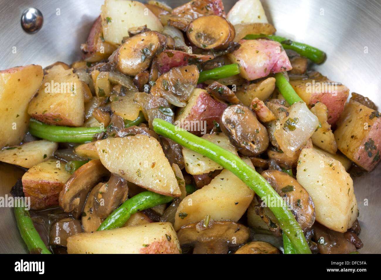 Une vue très étroite de la pommes de terre, haricots verts, oignons et champignons la cuisson dans une poêle en acier inoxydable. Banque D'Images