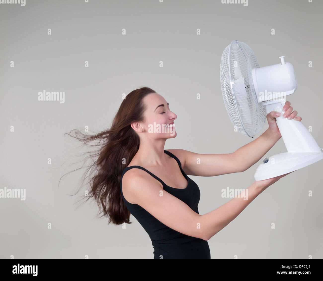 Jeune femme avec ventilateur électrique, smiling Banque D'Images