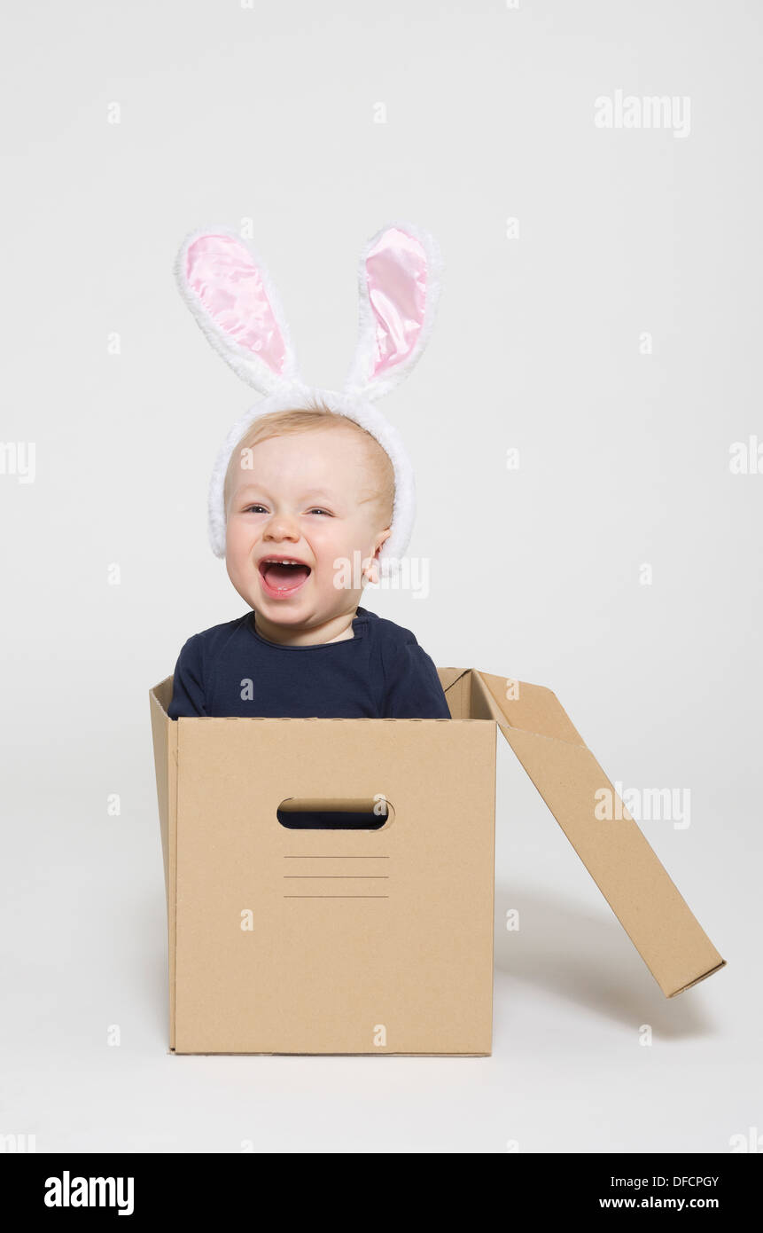 Bébé garçon portant des oreilles de lapin et assis dans la boîte, smiling Banque D'Images