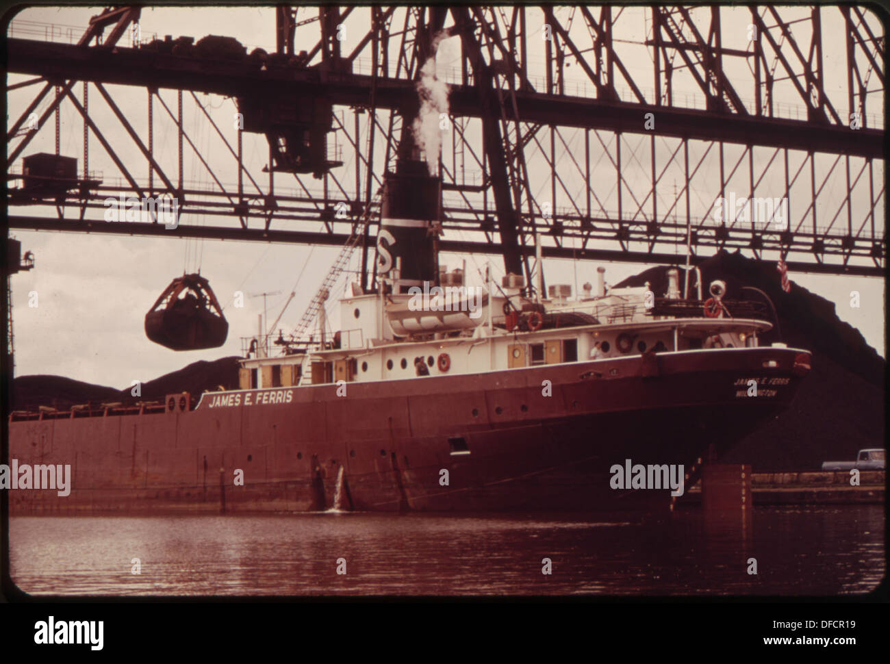 Le charbon est déchargé d'un cargo dans un canal adjacent à la Charmin Paper Company. Cette image met en évidence l'activité industrielle et le transport du charbon à des fins manufacturières. Banque D'Images