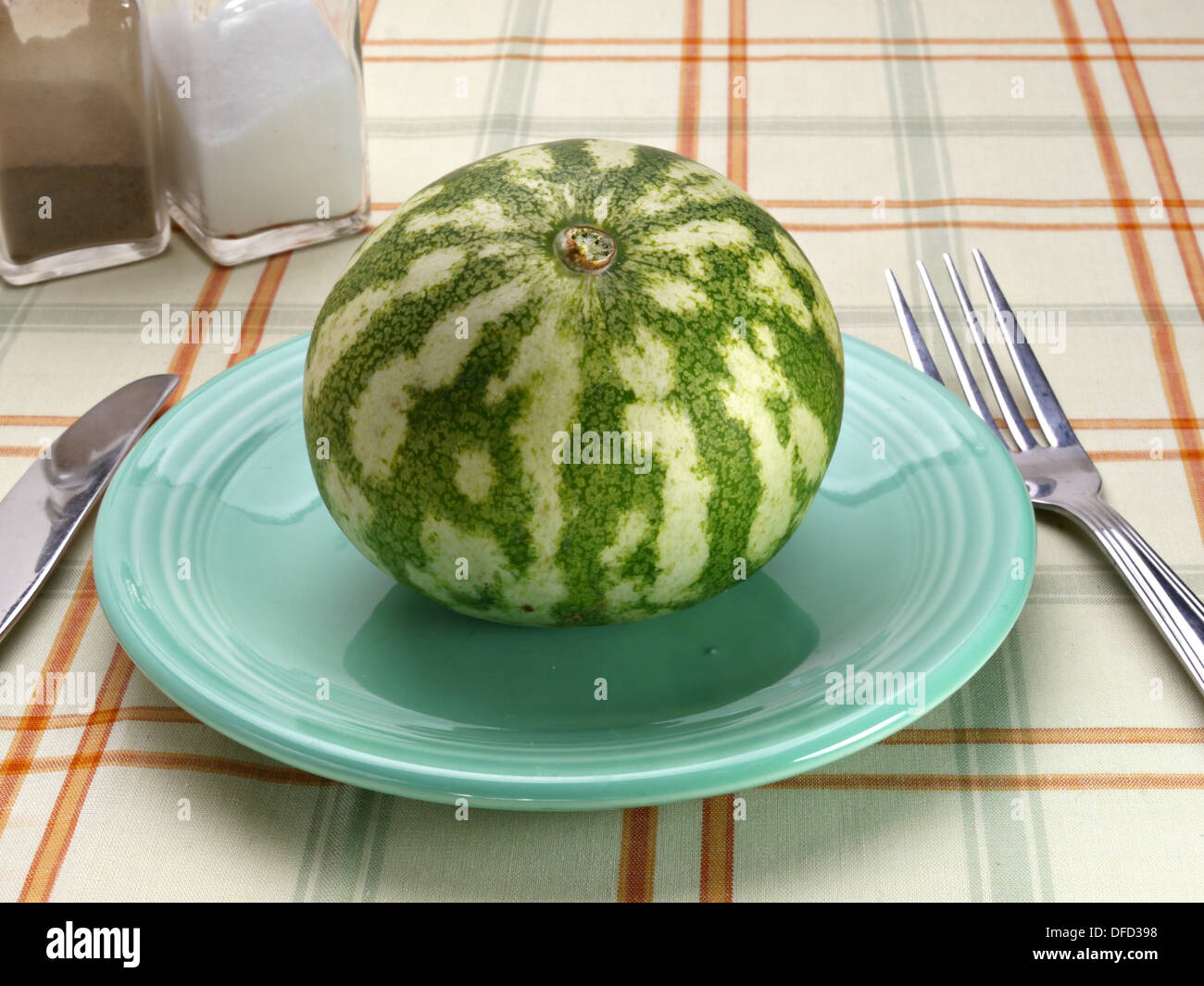 Un petit tour watermelon est assis sur une soucoupe volante bleu sur une table. Banque D'Images