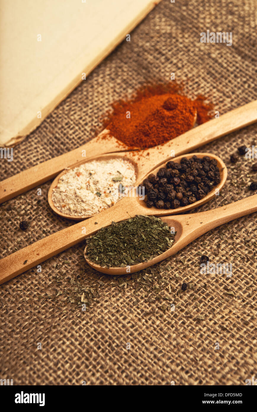 Les épices. Les ingrédients alimentaires des cuillères en bois avec livre ouvert sur la table de cuisine. Banque D'Images