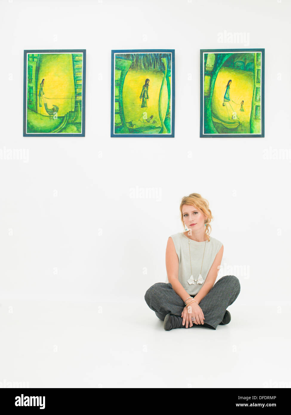 Vue avant du jeune femme assise sur un sol en face de peintures colorées affichées sur le mur, dans une galerie d'art Banque D'Images