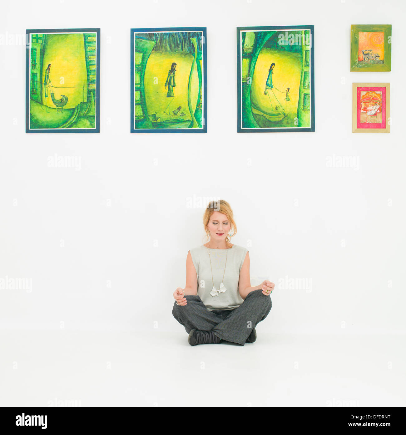 Vue de face de femme assise sur un étage dans une posture de méditation appuyé contre un mur de peintures colorées Banque D'Images