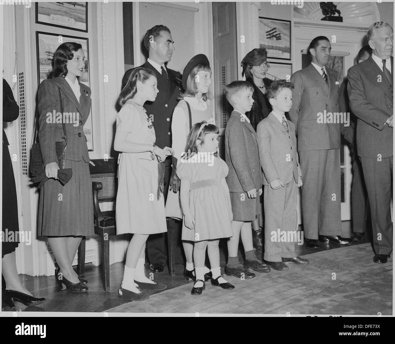 Les membres de la famille de W. John Kennedy et John L. Sullivan, des fonctionnaires de la marine américaine, observent un événement important dans un cadre de bureau ovale. Ce moment saisit un aperçu de la vie de personnalités navales de haut rang au cours d'une occasion historique. Banque D'Images