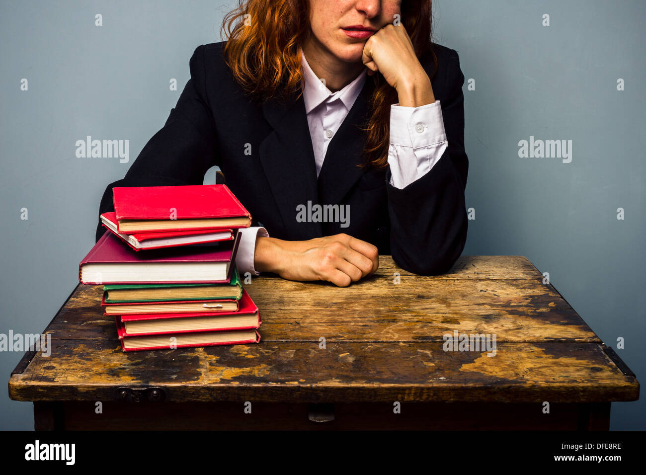 Young businesswoman sitting at desk with pile de livres s'ennuie Banque D'Images