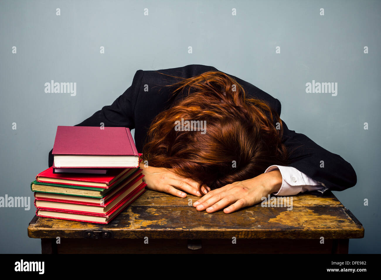 Young businesswoman est endormi au bureau avec une pile de livres en face d'elle Banque D'Images