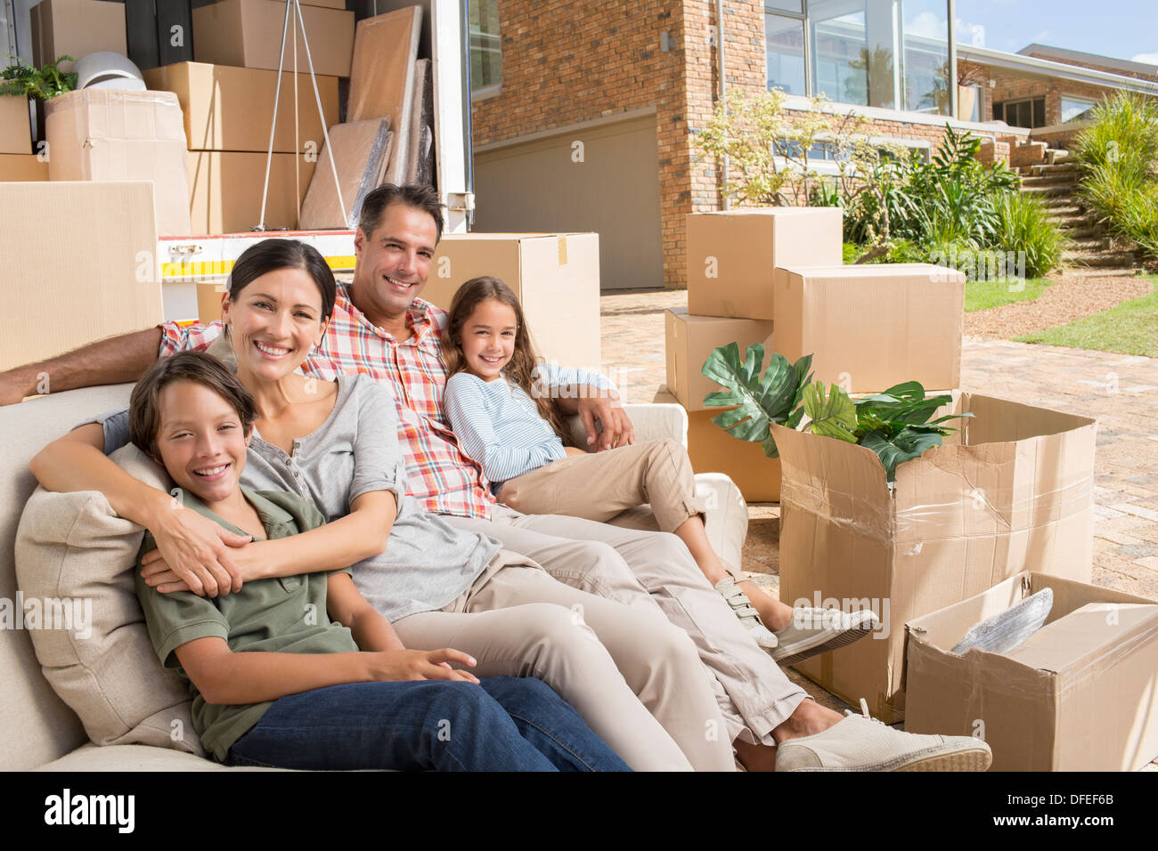 Portrait of smiling family sitting on sofa près de camion de déménagement en entrée Banque D'Images
