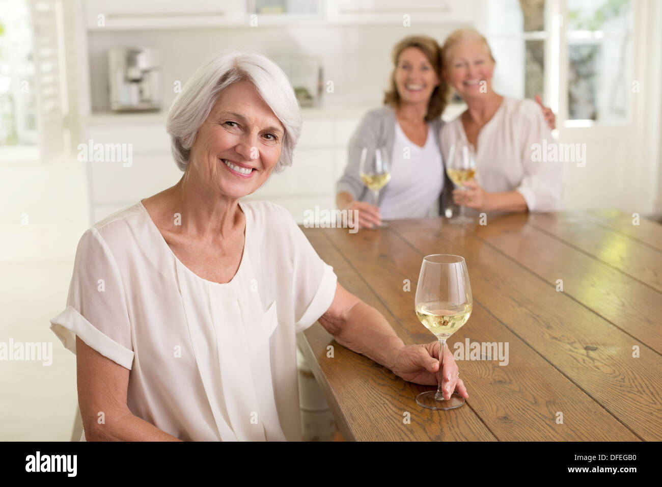 Les femmes âgées drinking white wine in kitchen Banque D'Images