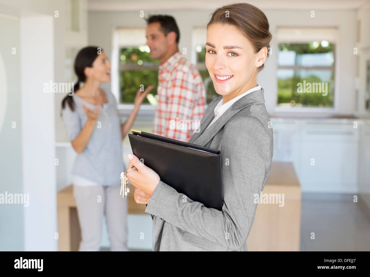 Portrait of smiling couple avec de l'agent immobilier en arrière-plan Banque D'Images