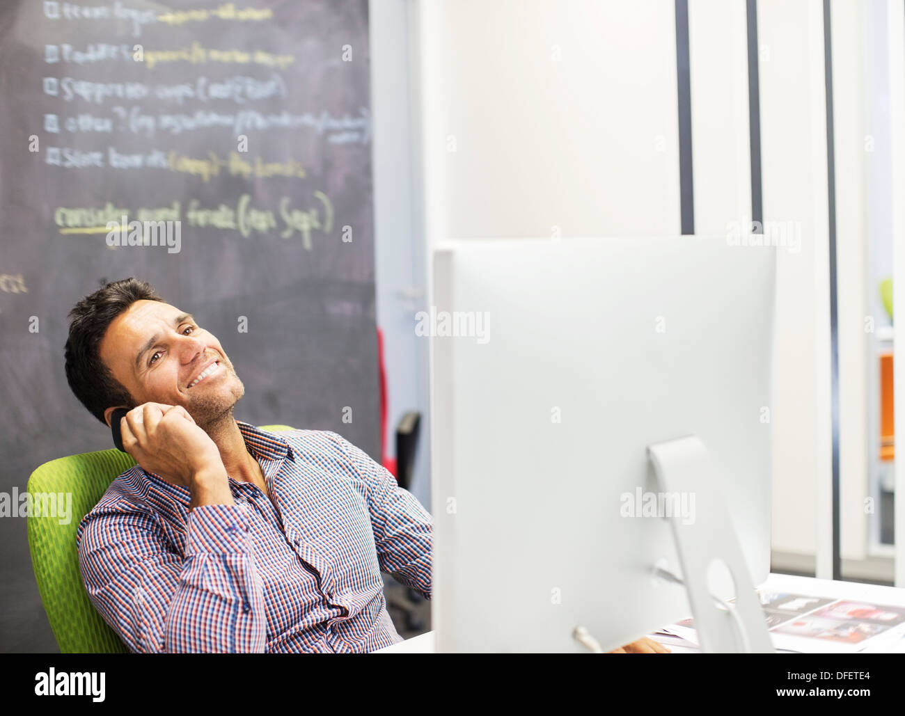 Businessman talking on cell phone at desk in office Banque D'Images