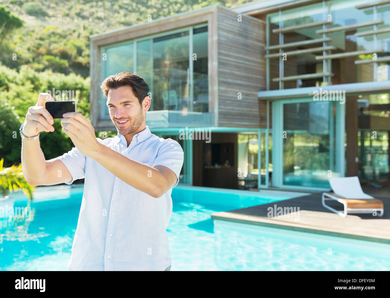 Man taking self-portrait with camera phone at poolside Banque D'Images