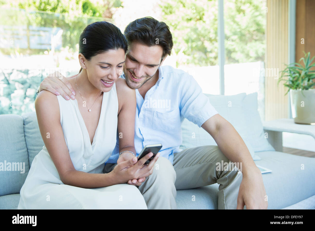 Couple using cell phone on sofa Banque D'Images