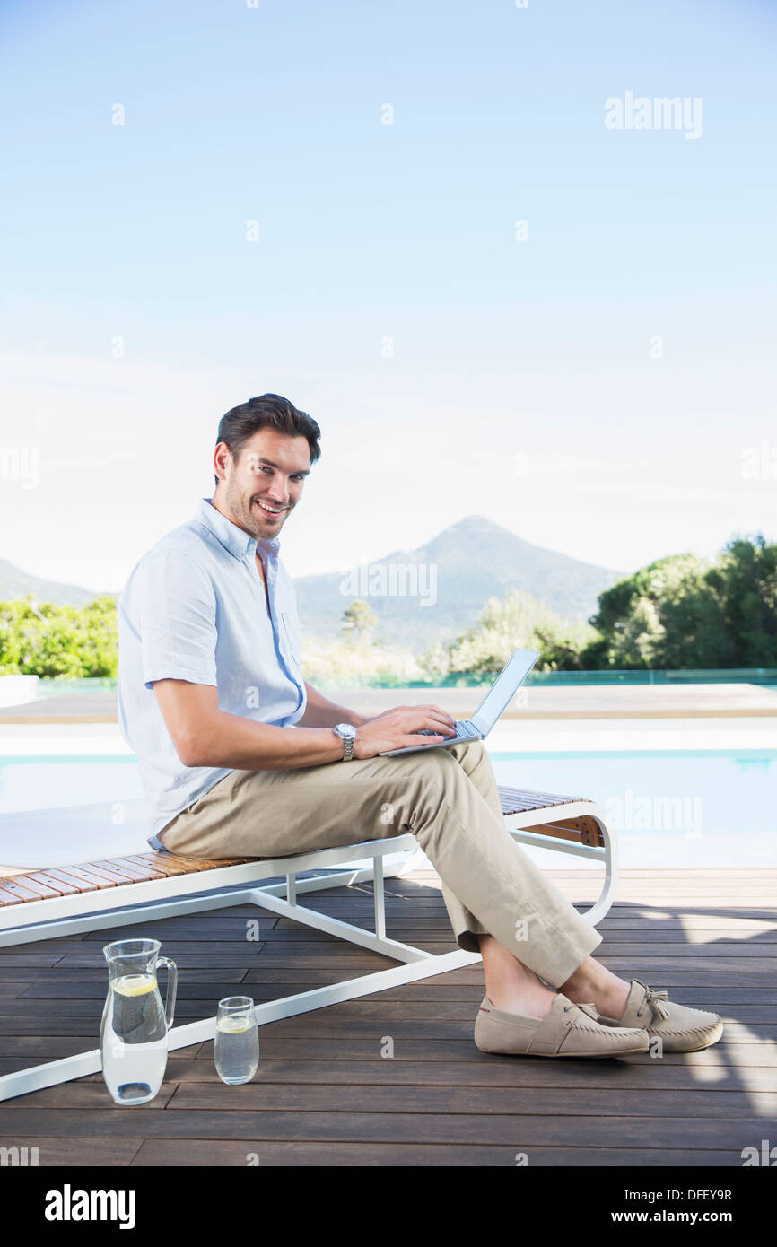 Man using laptop on lounge chair at poolside Banque D'Images