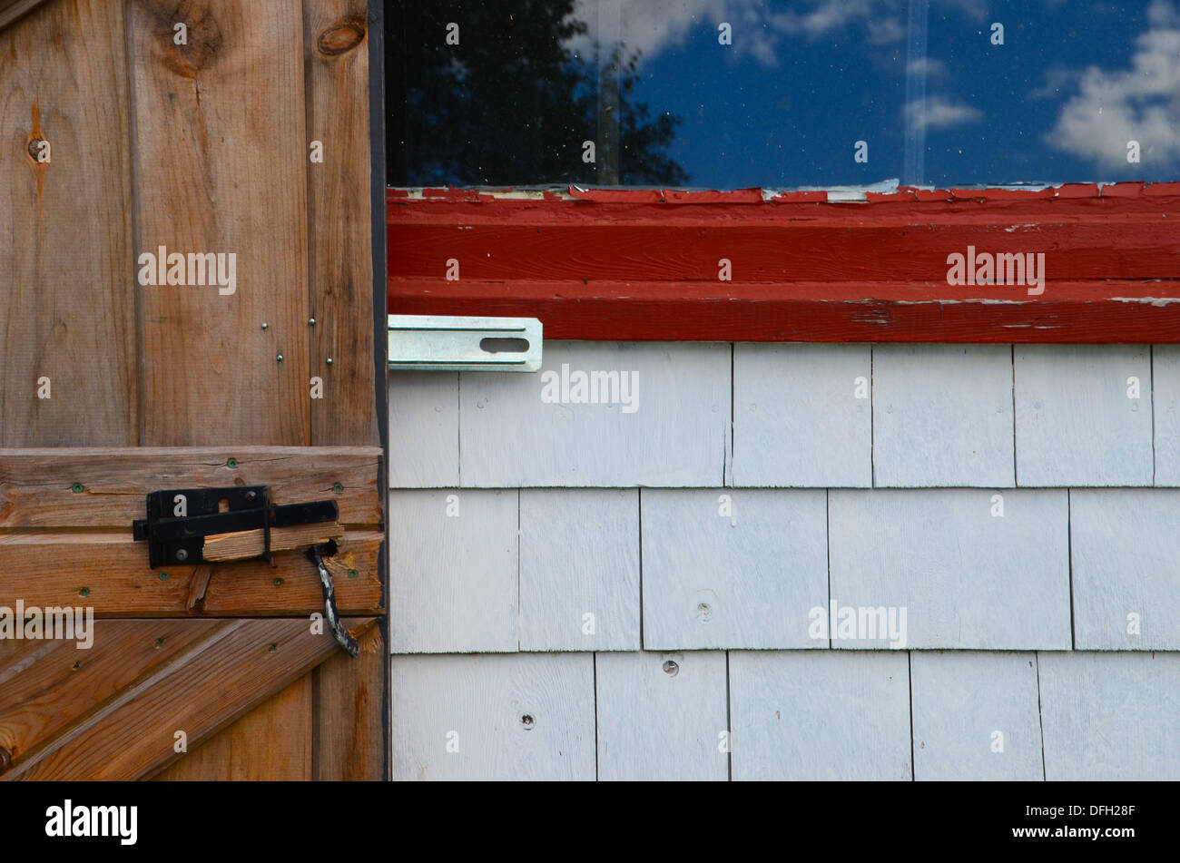 Moyenne géométrique photo d'une porte de grange en bois brun contre white barn bardeaux, châssis de fenêtre rouge et un ciel bleu, la réflexion de la fenêtre Banque D'Images