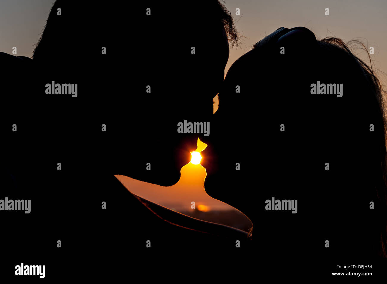 Silhouette de jeune couple avec soleil entre leurs lèvres Banque D'Images