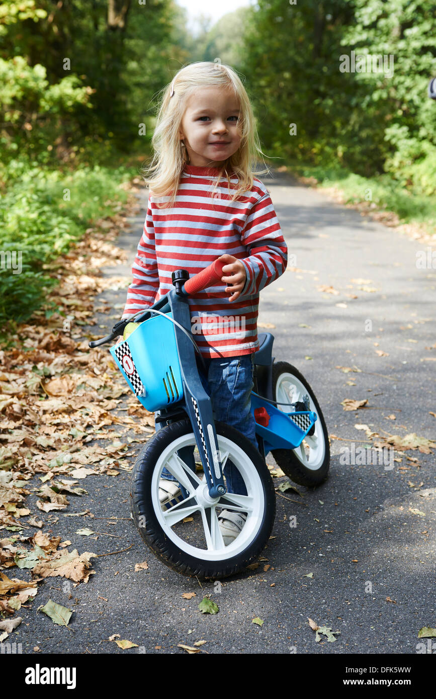 L'équilibre de l'enfant blond girl riding Bike in forest road, l'été Banque D'Images