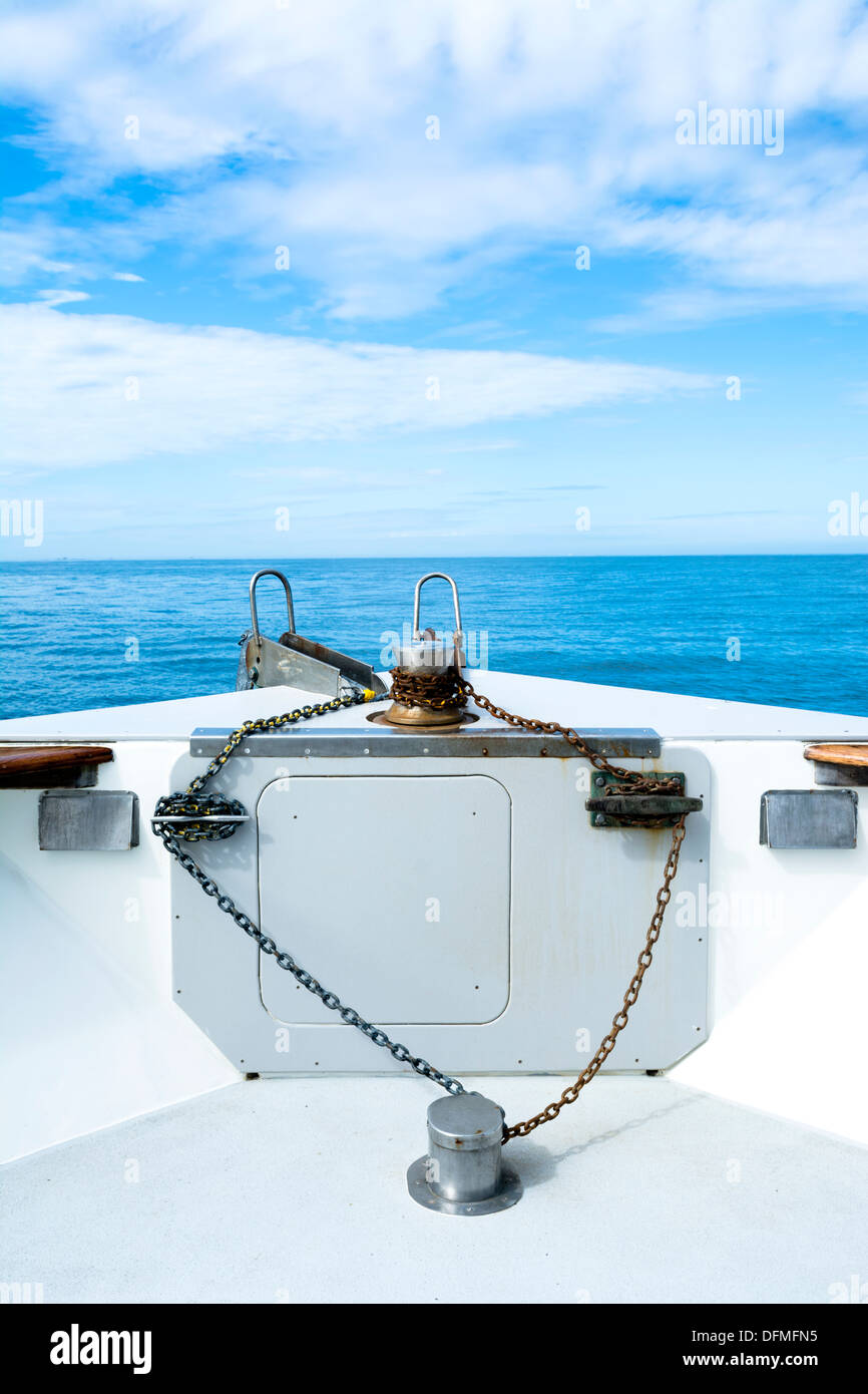 La proue d'un bateau de croisière affiche sa chaîne d'ancre rouillée, écarteurs et winch entre un ciel bleu et des îles lointaines. Banque D'Images