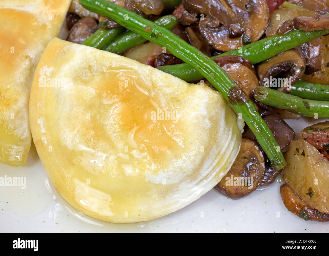 Une vue étroite d'un repas cuit des pierogies avec haricots verts, champignons, oignons et pommes de terre rouge sur une assiette. Banque D'Images