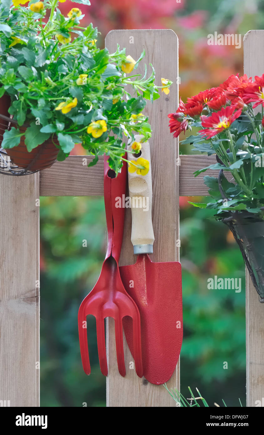 Outils de jardinage et pot de fleur suspendu à une clôture Banque D'Images