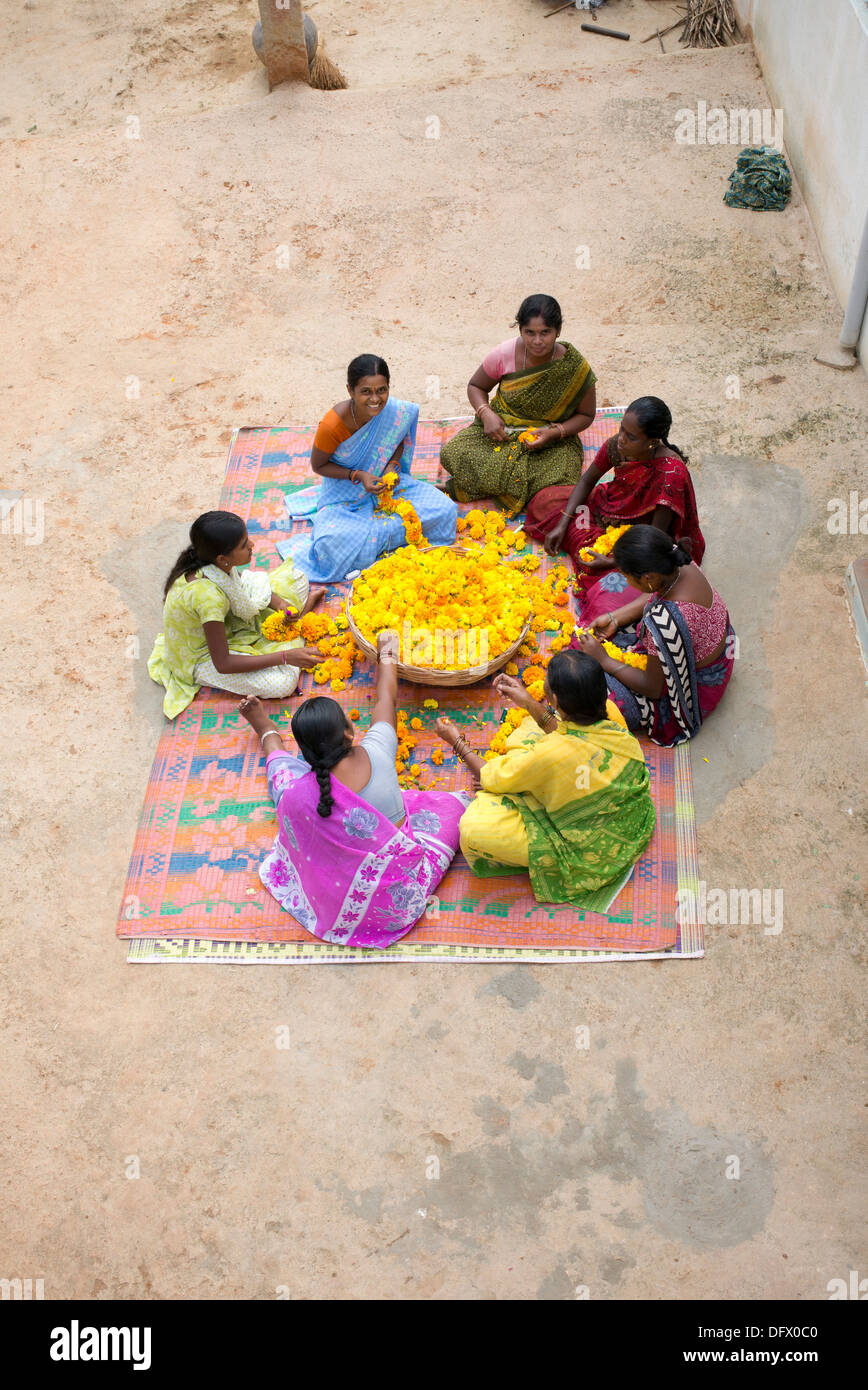 Les femmes du village de l'Inde rurale assis autour d'un panier de fleurs de souci de faire des guirlandes de fleurs. L'Andhra Pradesh, Inde Banque D'Images