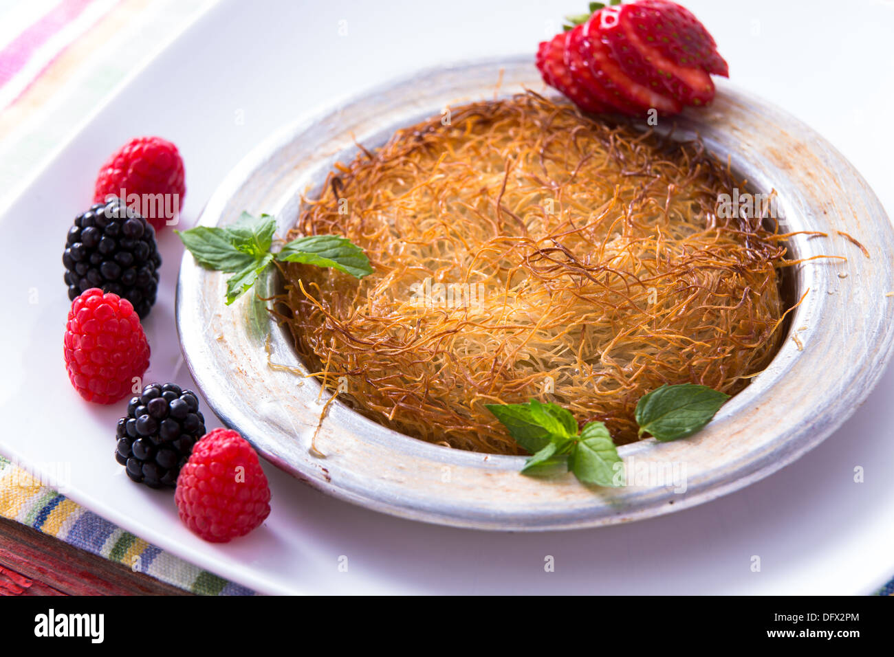 Kunefe dessert turc servi dans la plaque d'aluminium sur une plaque blanche avec la menthe et fraise en tranches le long rouge et noir Banque D'Images