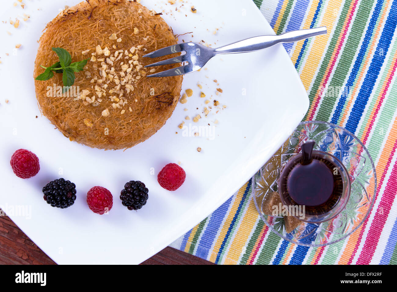 Kunefe dessert turc servi sur une plaque blanche avec les feuilles de menthe le long de baies rouges et noires sur une table de pique-nique Banque D'Images