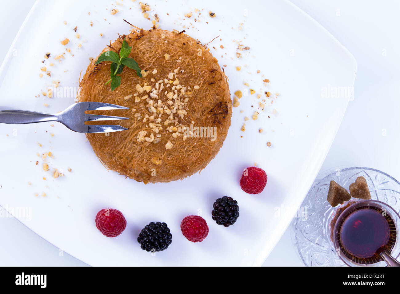 Kunefe dessert turc servi sur une plaque blanche avec des feuilles de menthe, de baies rouges et noires avec du thé chaud turc Banque D'Images