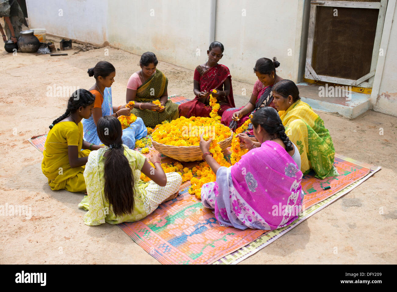 Les femmes du village de l'Inde rurale assis autour d'un panier de fleurs de souci de faire des guirlandes de fleurs. L'Andhra Pradesh, Inde Banque D'Images